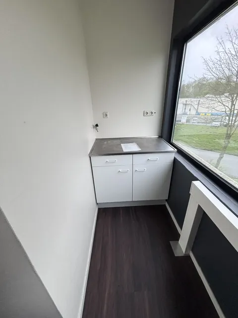 Een smalle ruimte vóór de verbouwing met een wit keukenblok onder een groot raam