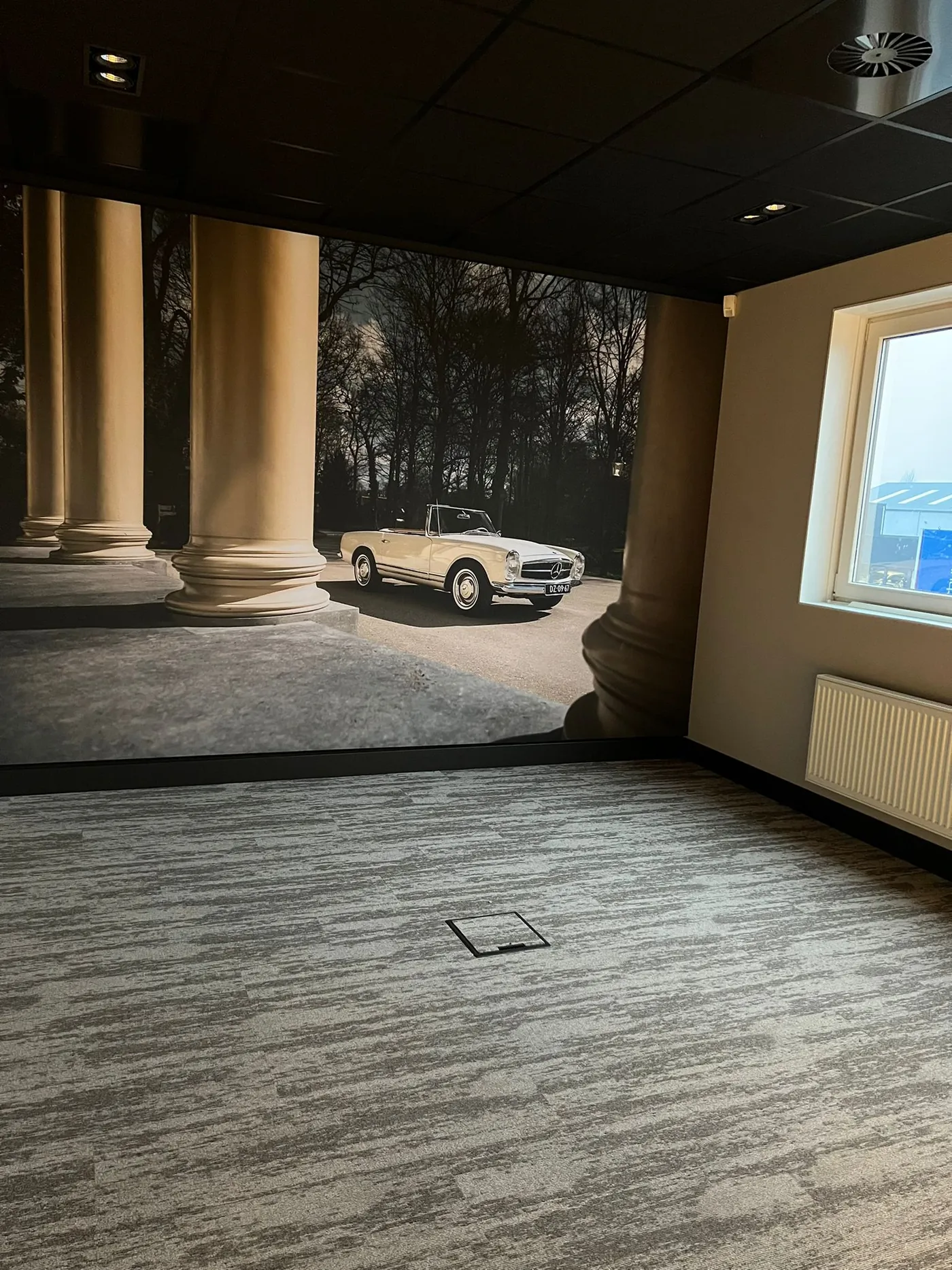 Een lege ruimte in aanbouw met een wandvullende print van een klassieke cabriolet