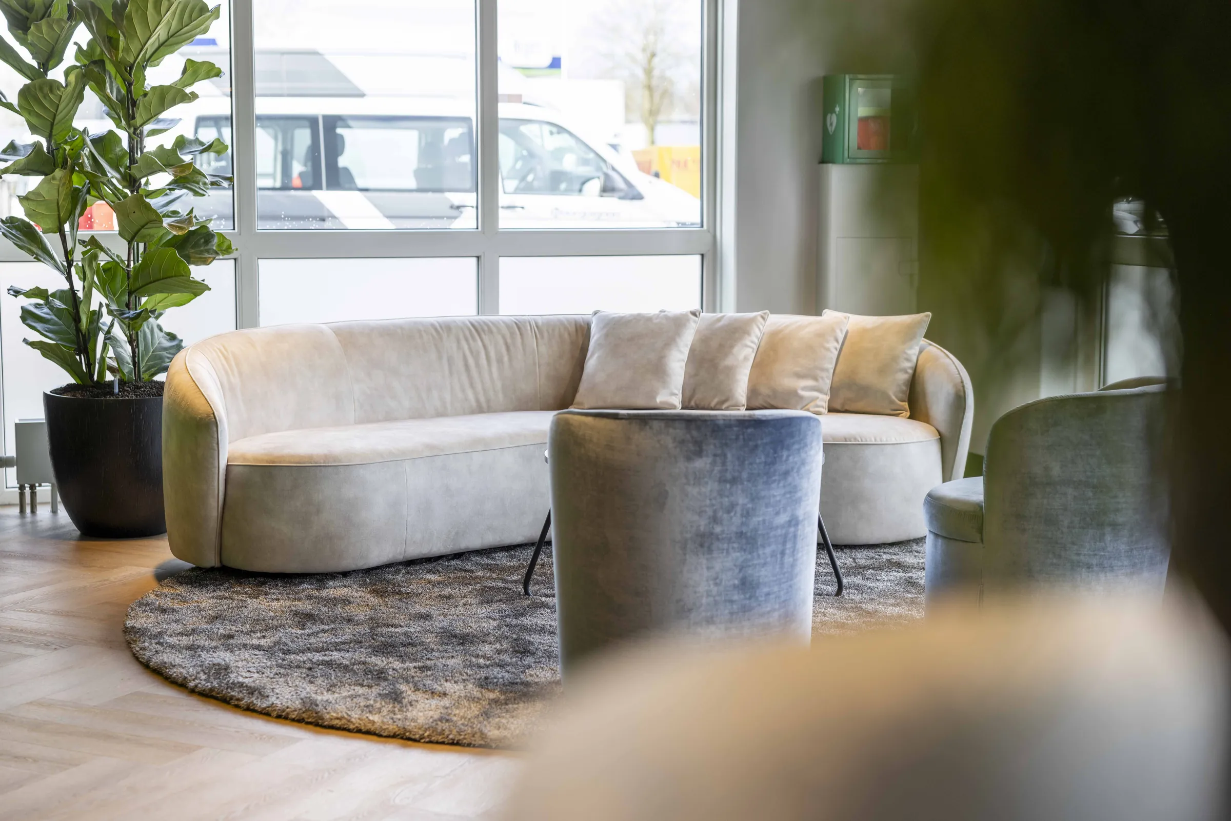 Loungehoek met ronde bank, zachte kussens en een groot groen blad op de voorgrond