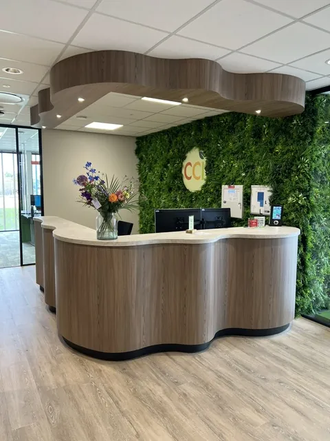 De golvende houten balie onder een golvend plafond, voor een moswand met het CCI-logo en een bos bloemen