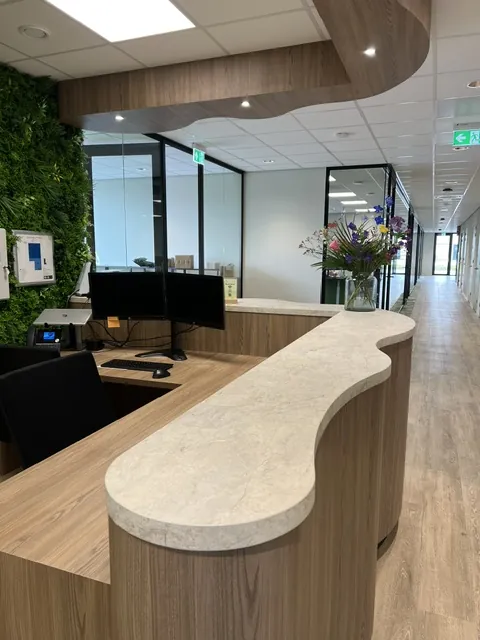 De balie van dichtbij, met een golvend blad in lichte steenlook op een houten front en doorkijk naar de gang