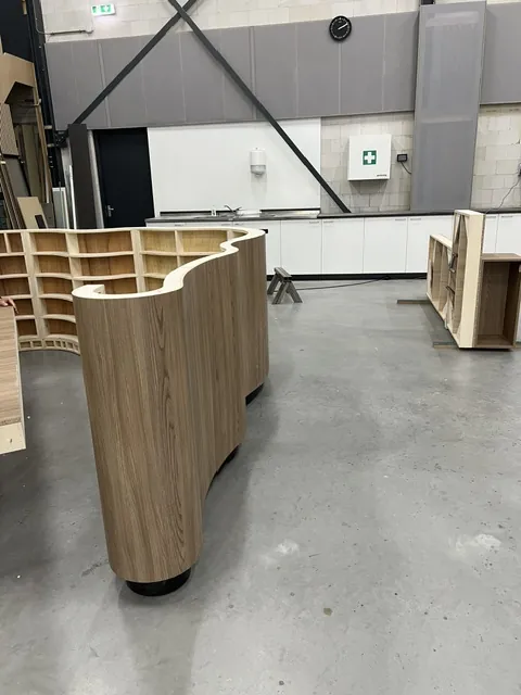 De golvende balie in aanbouw in de werkplaats, met open kasten op een betonvloer