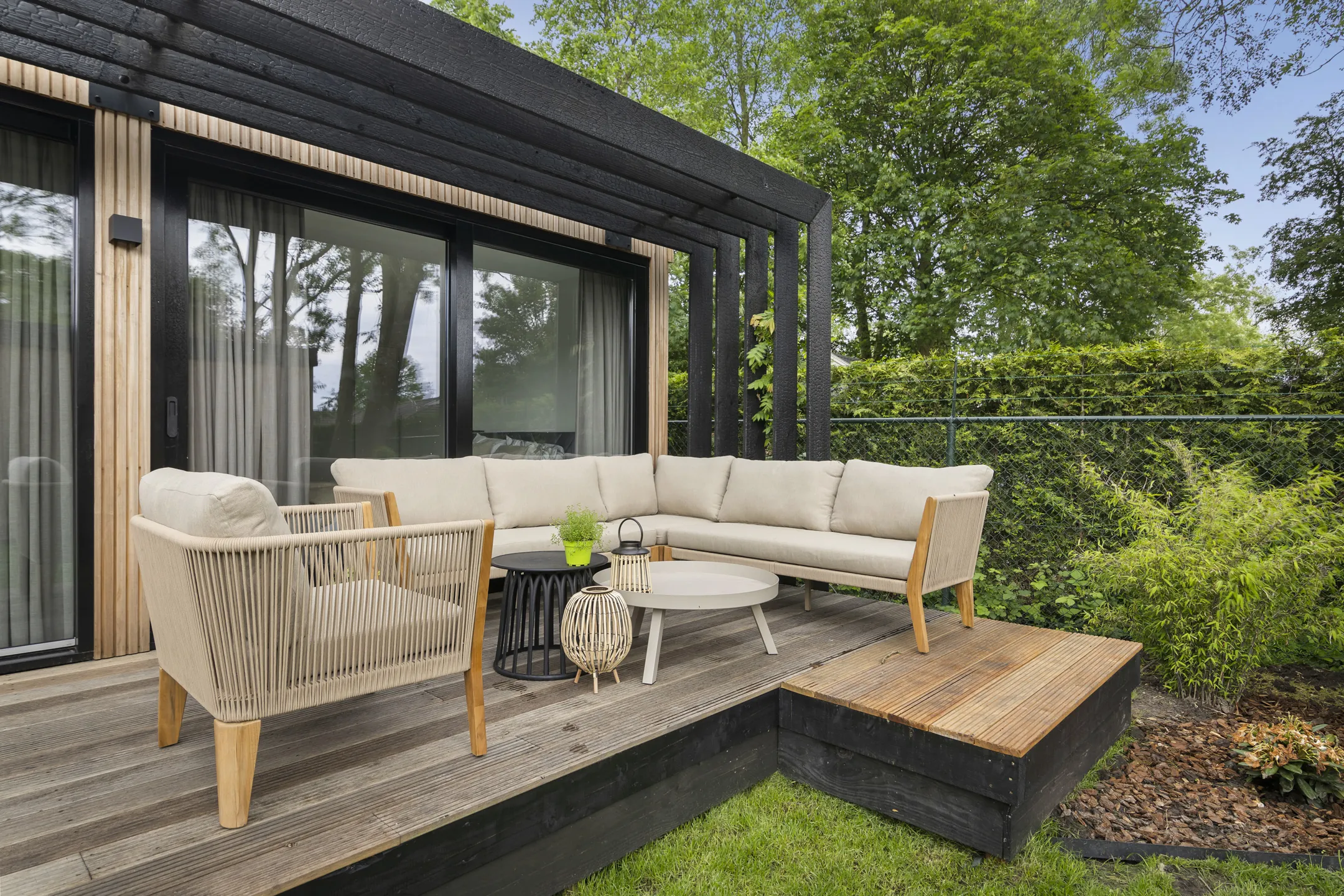 Het terras onder de zwarte pergola, met een loungebank en een fauteuil