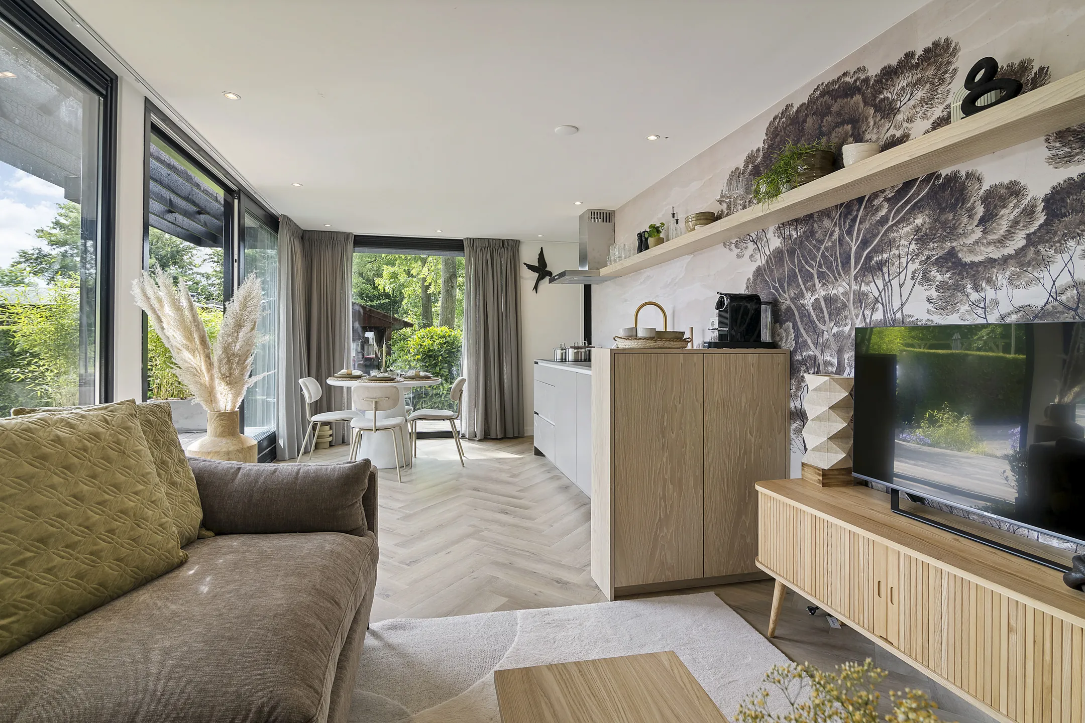 De opgeleverde woonkamer in het vakantiechalet in Grou, met hetzelfde bomenbehang en een houten tv-meubel
