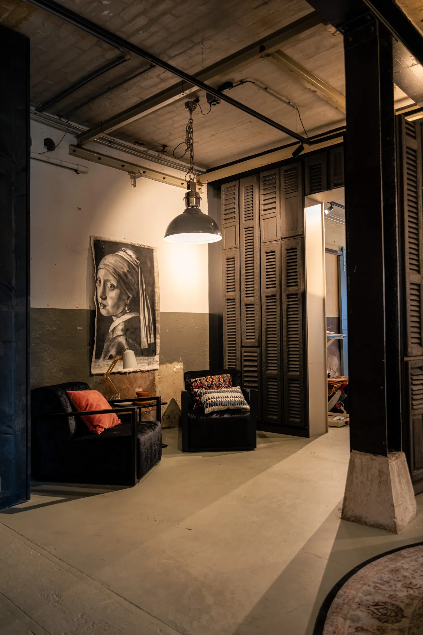 Zithoek met twee zwarte fluwelen fauteuils, een industriële hanglamp en een houtskooltekening aan de wand