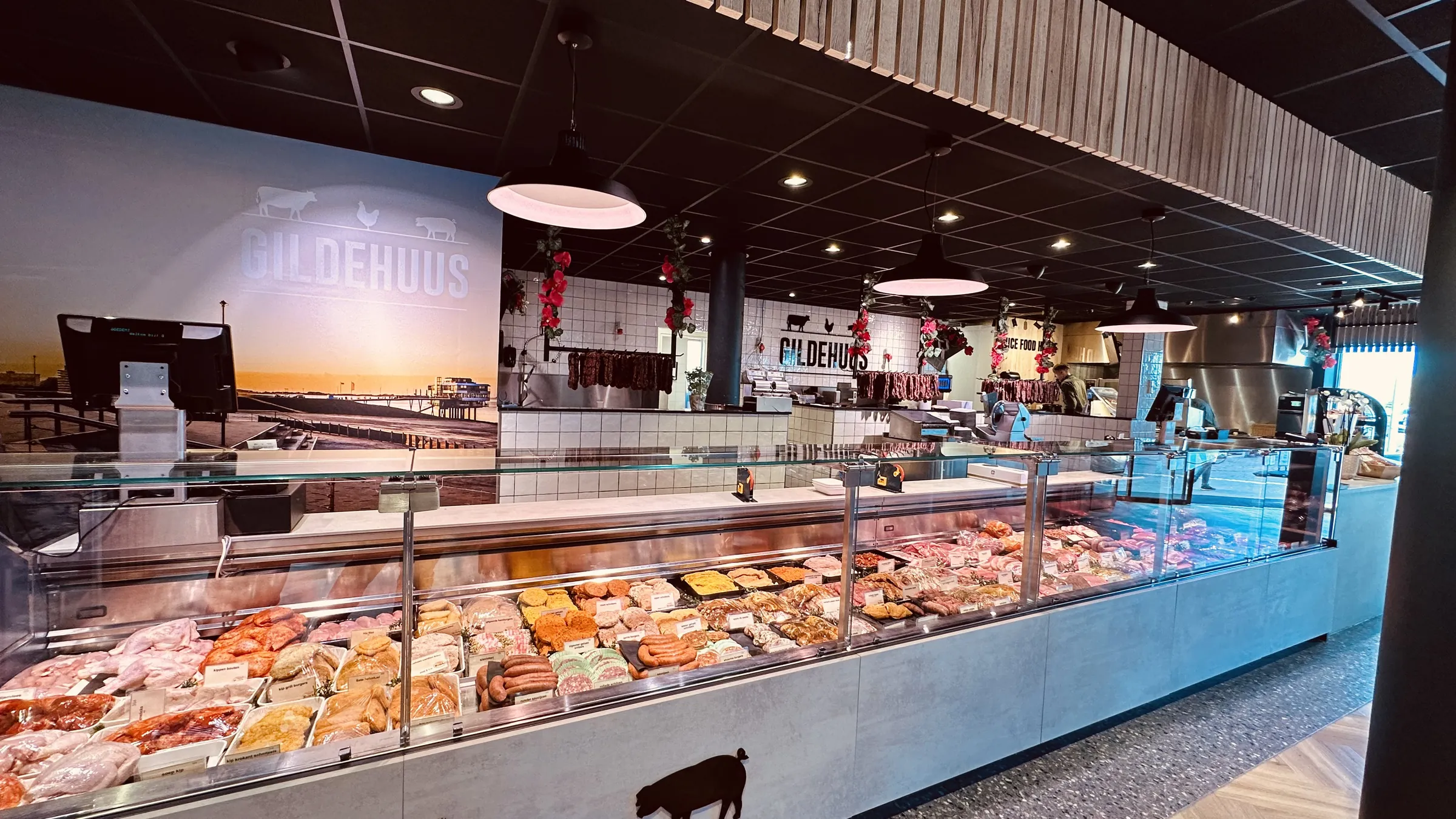 Lange koelvitrine vol vleeswaren voor een fotowand met het Gildehuus-logo, een pier en een zonsondergang