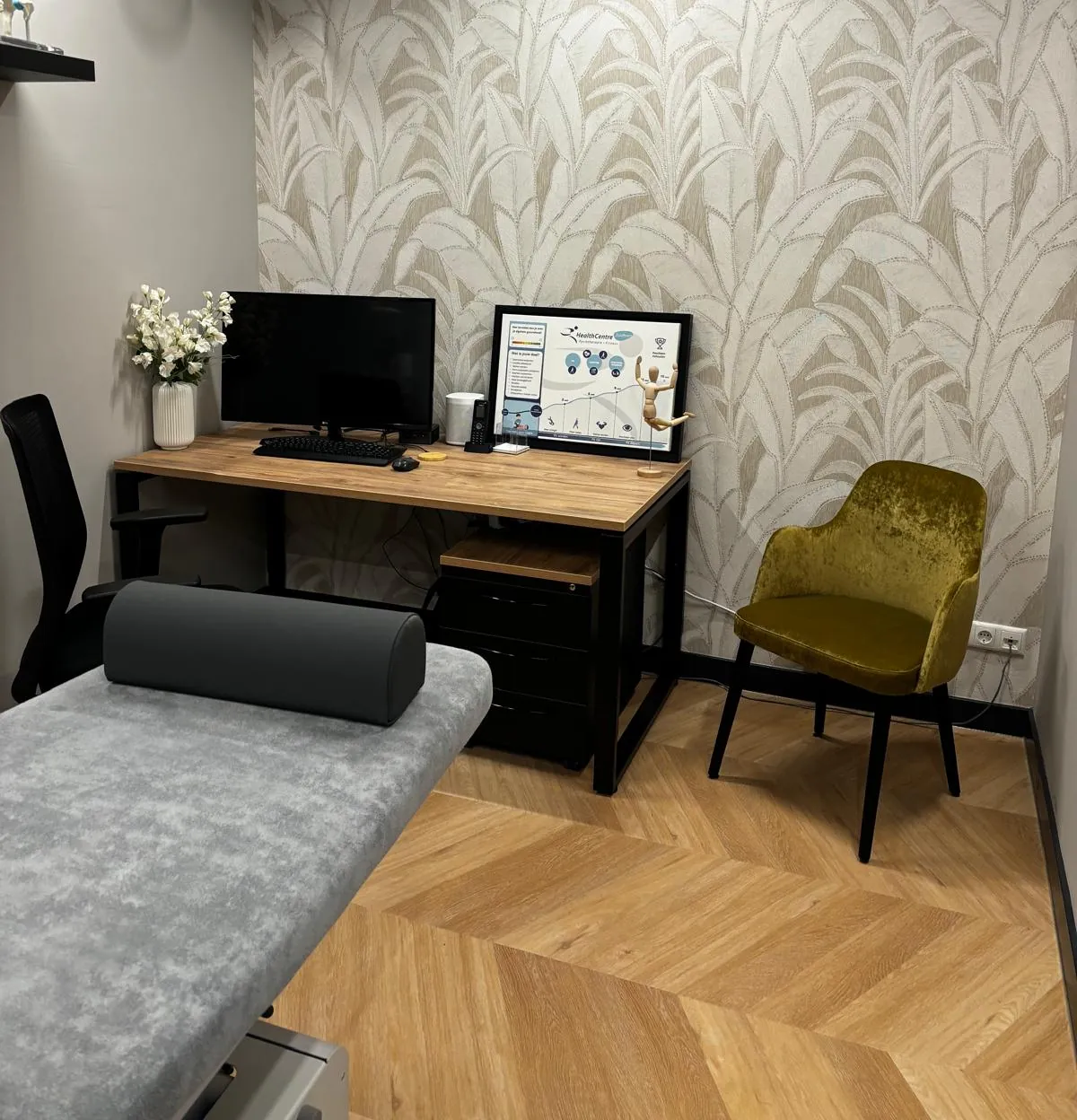 Bureauhoek van een behandelkamer met palmbladbehang, een groene fluwelen stoel en een poster van HealthCentre