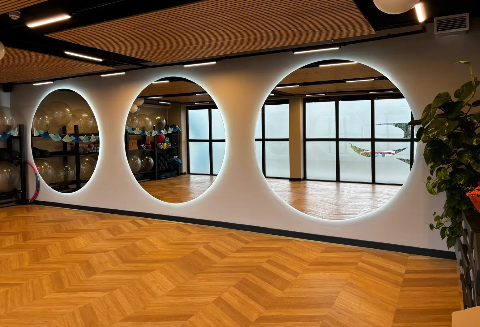 Groepszaal met drie grote ronde spiegels met ledrand, een visgraatvloer en een houten lamellenplafond met lijnverlichting