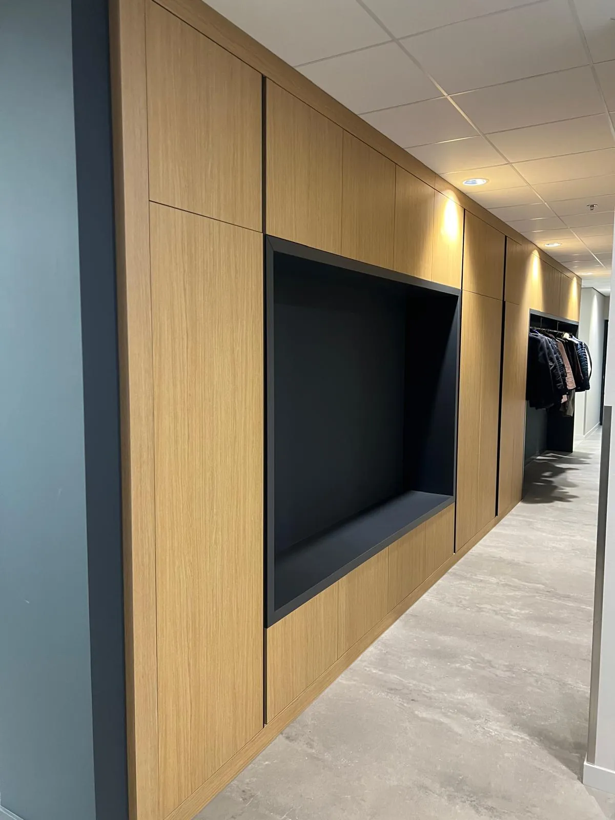 Gang met een wand van eiken kasten rond een donkere nis, met achterin de garderobe