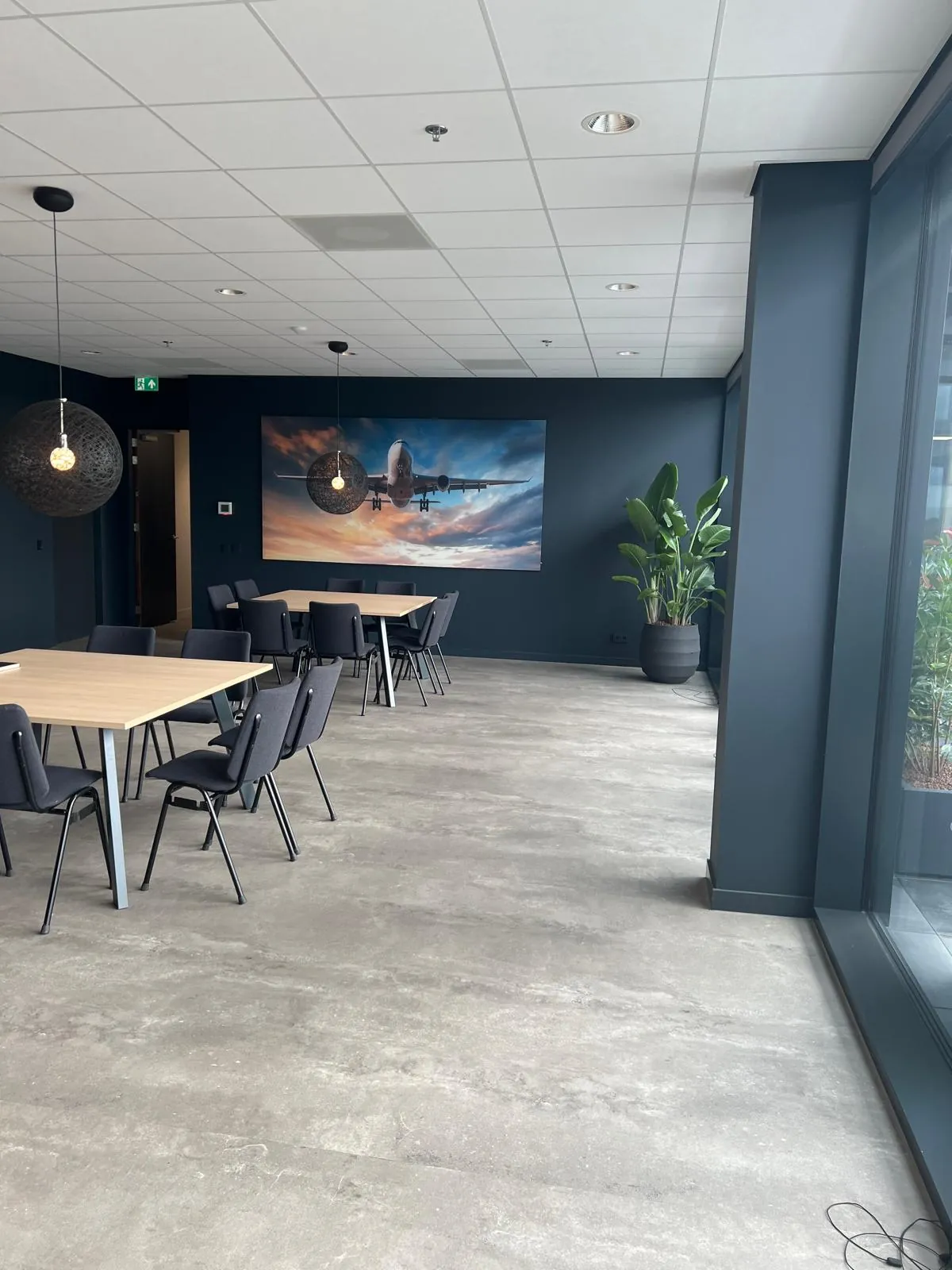 Kantine met eiken tafels, donkere stoelen, bolvormige hanglampen en een grote vliegtuigfoto aan de wand