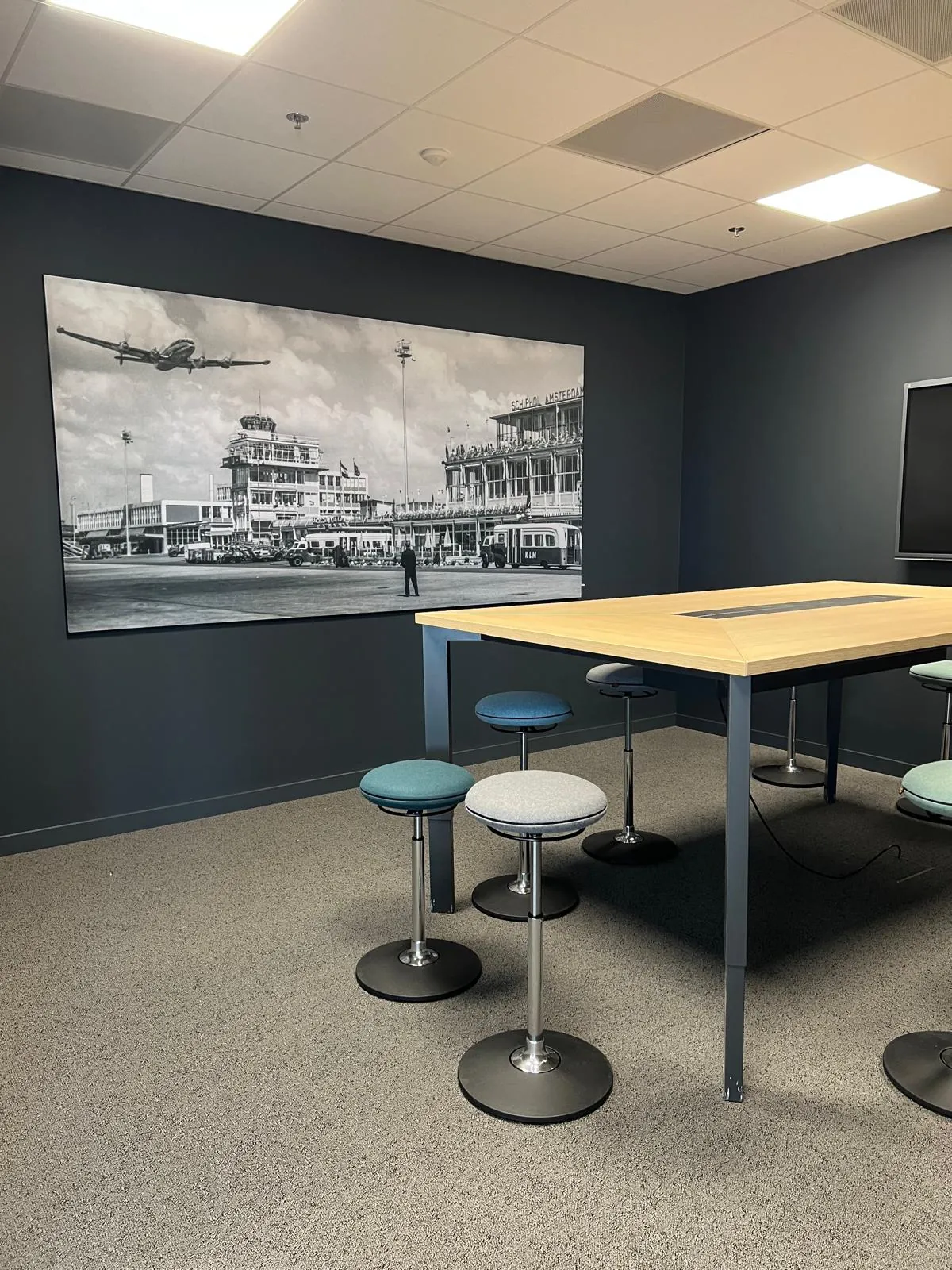 Vergaderruimte met een eiken tafel en krukken voor een grote zwart-witfoto van het oude Schiphol