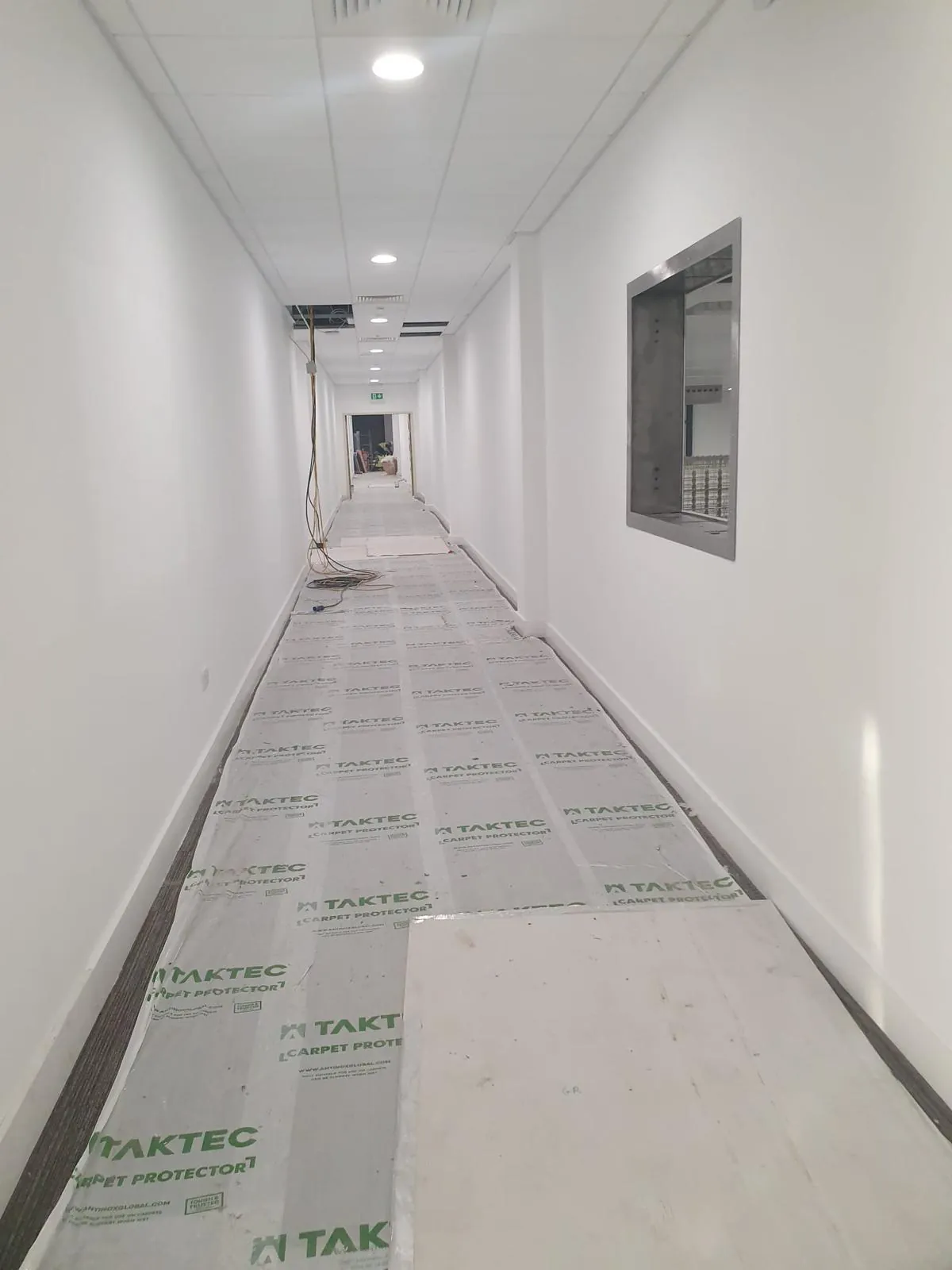 Gang tijdens de bouw met een afgedekte vloer, losse kabels en een deels open plafond