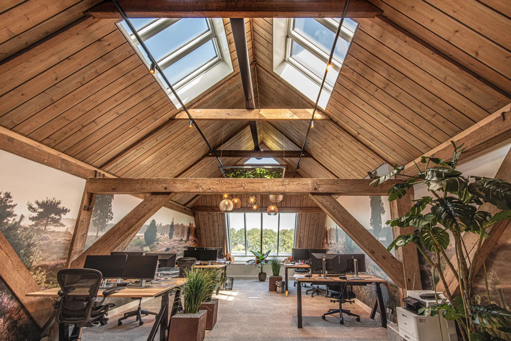 De opgeleverde zolder met werkplekken, planten en landschapsbeelden op de wand