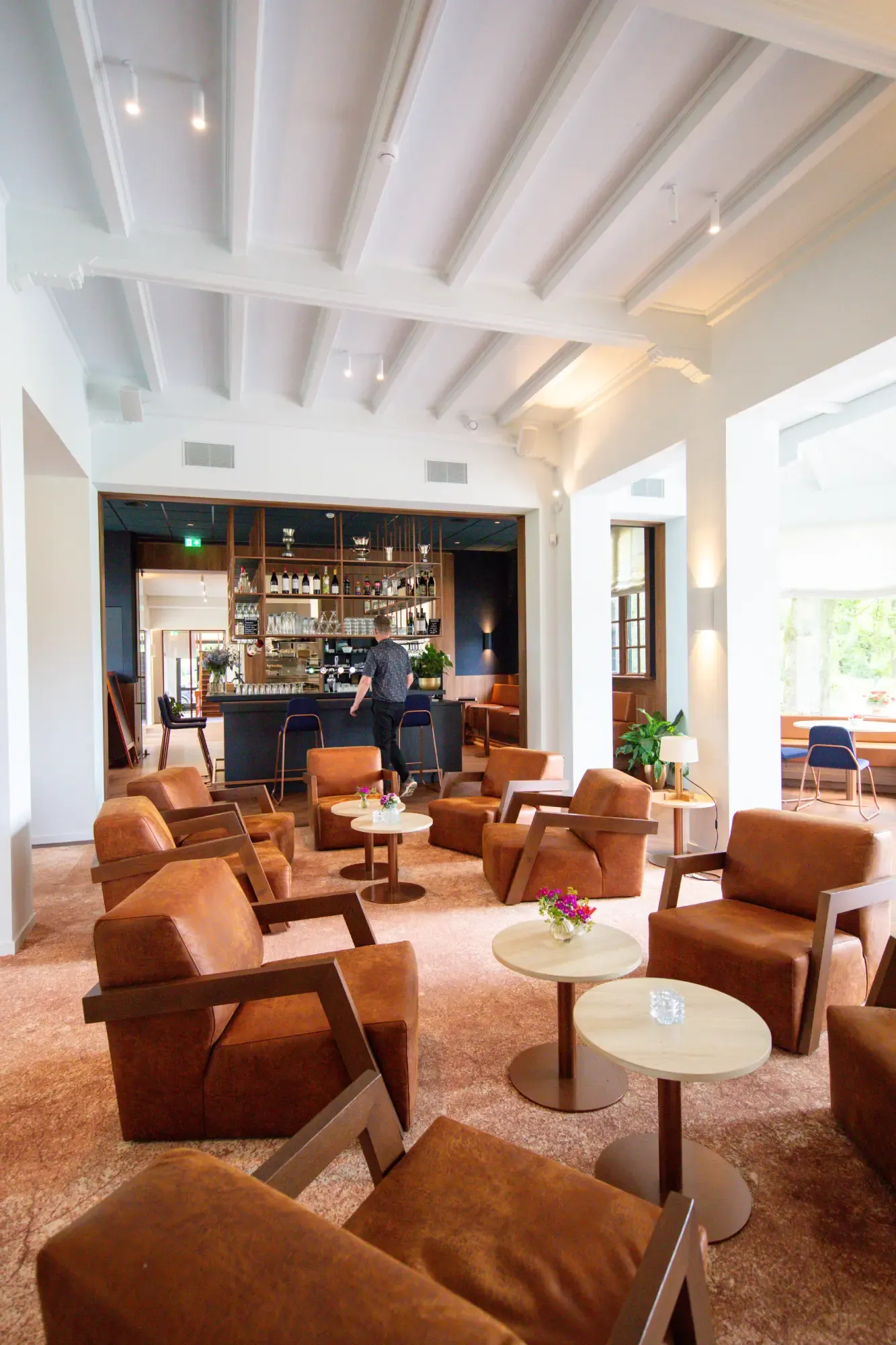 Leren fauteuils en ronde tafeltjes voor de bar van het clubhuis