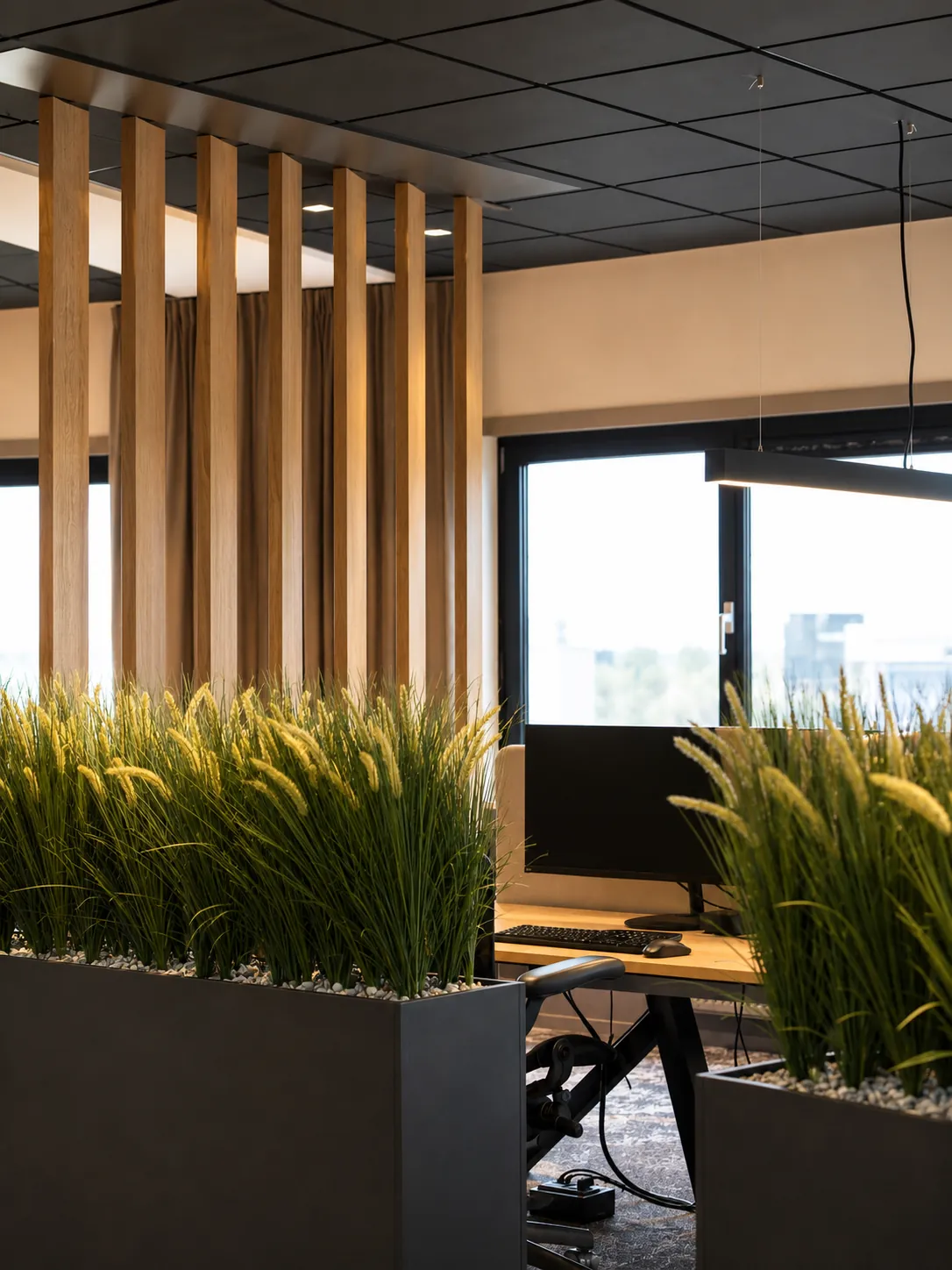 Verticale eiken lamellen en zwarte plantenbakken met siergras bij een werkplek aan het raam