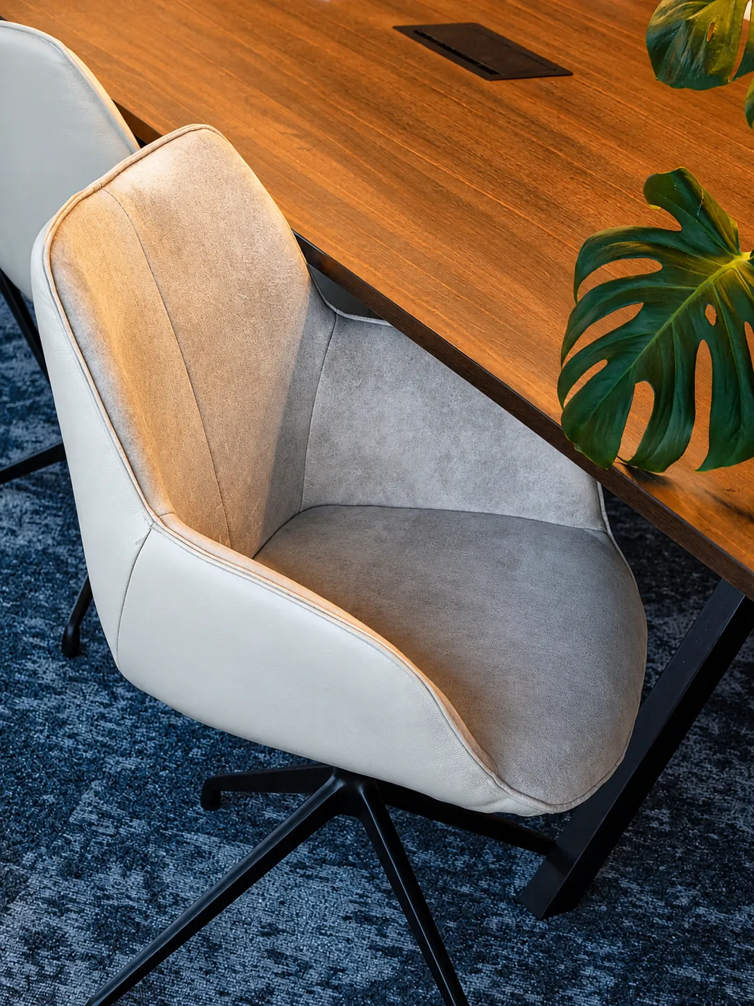 Een lichte leren vergaderstoel aan een houten tafel, met een monsterablad op de voorgrond