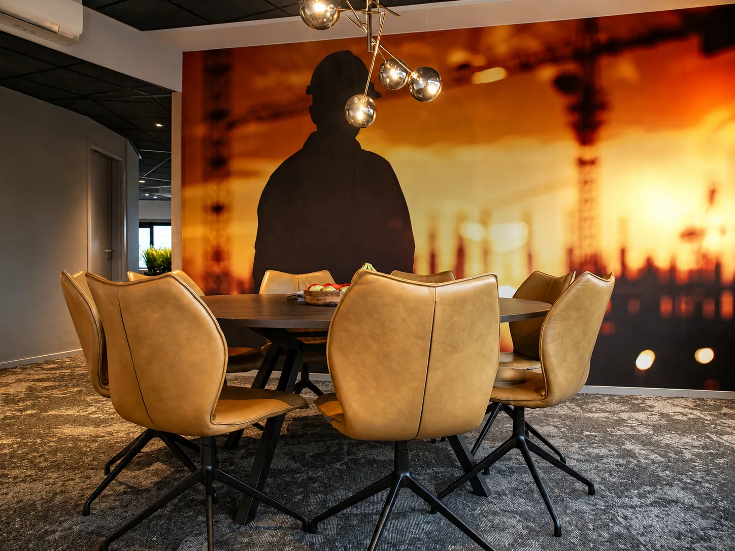 Ronde vergadertafel met cognackleurige stoelen en een gouden bollenlamp voor fotobehang met het silhouet van een bouwvakker