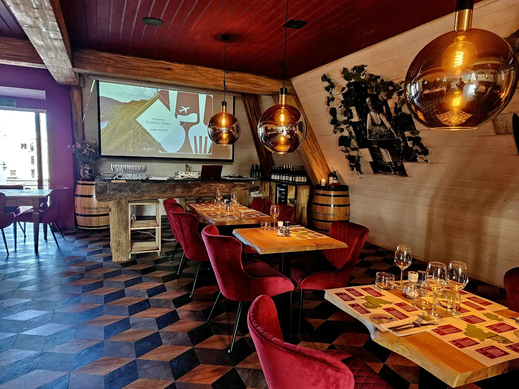 De wijnzolder met rode stoelen, gedekte tafels en een projectiescherm op de achterwand