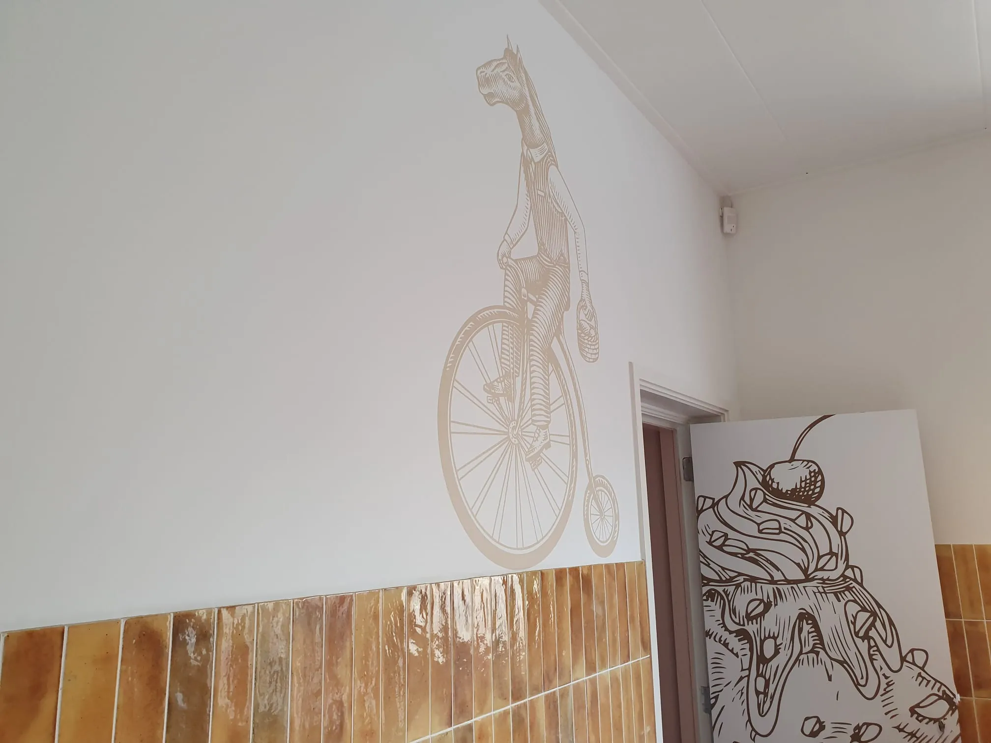 Een tekening van een paard op een hoge fiets op de witte muur, met een beplakte deur ernaast