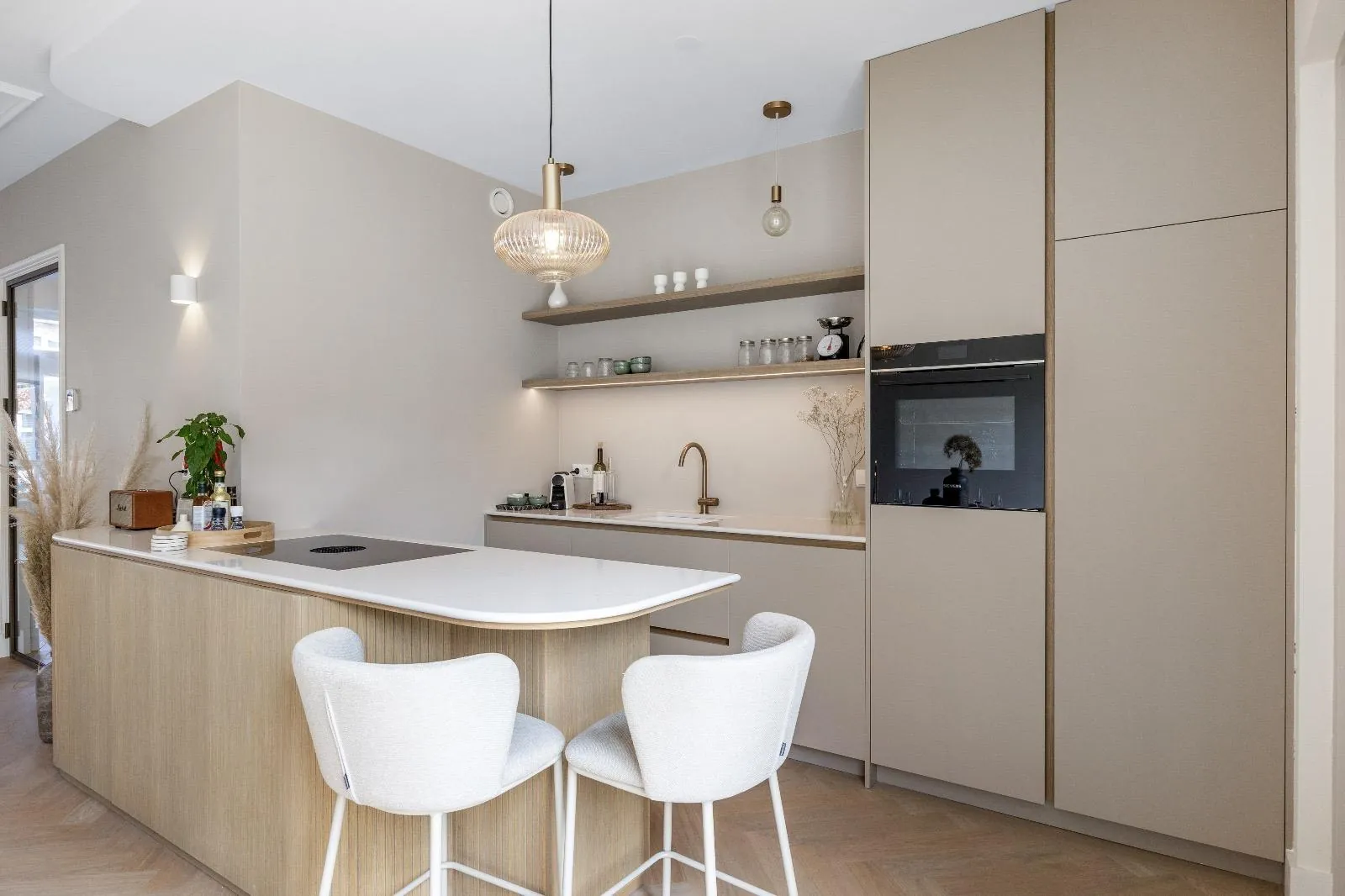 Keuken met een rond eindigend schiereiland, hoge greeploze kasten met inbouwoven en zwevende houten planken met ledverlichting