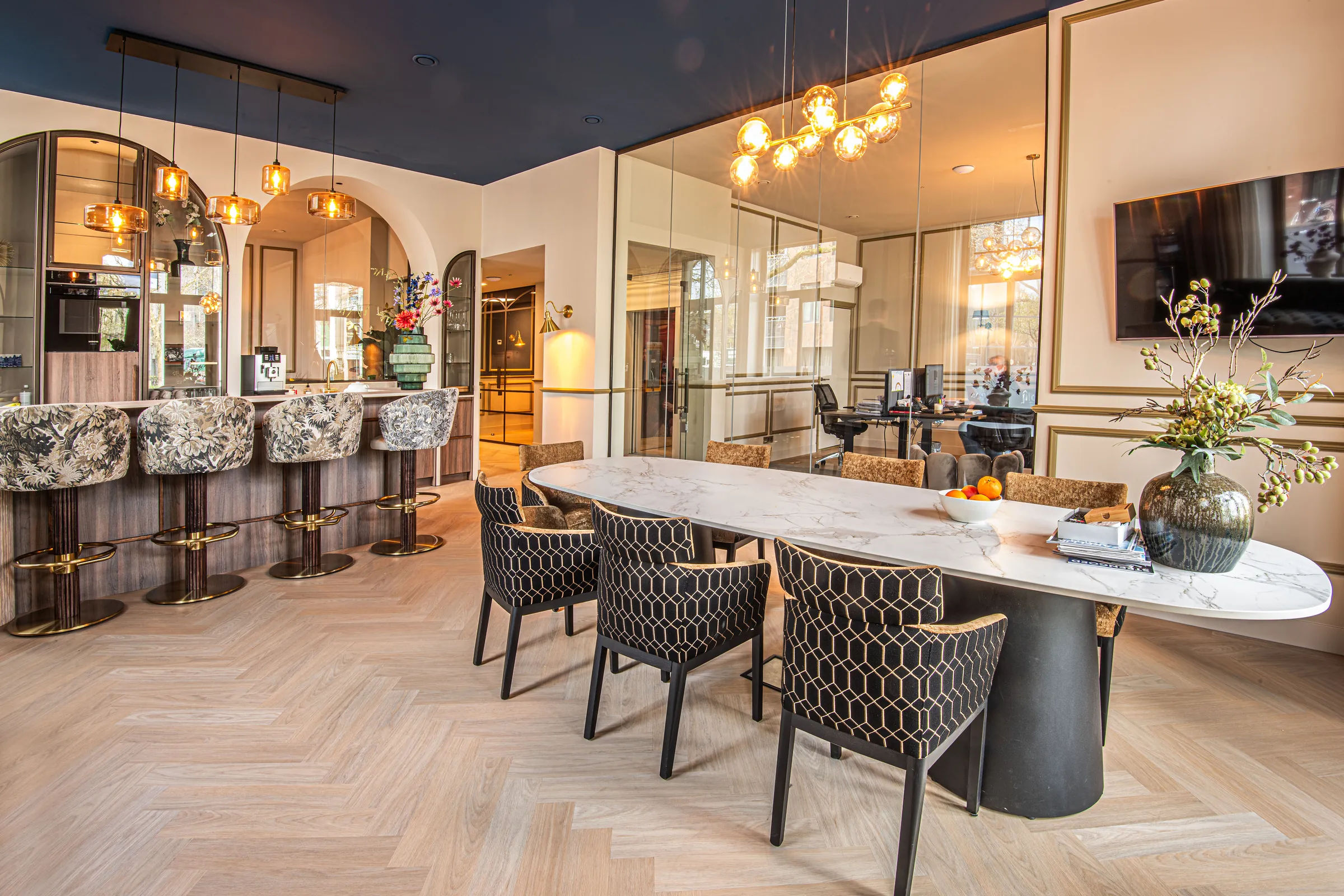 De lounge van Villa de Kroon in Leeuwarden: een ovale tafel met stoelen in honingraatpatroon en een bar onder een donkerblauw plafond